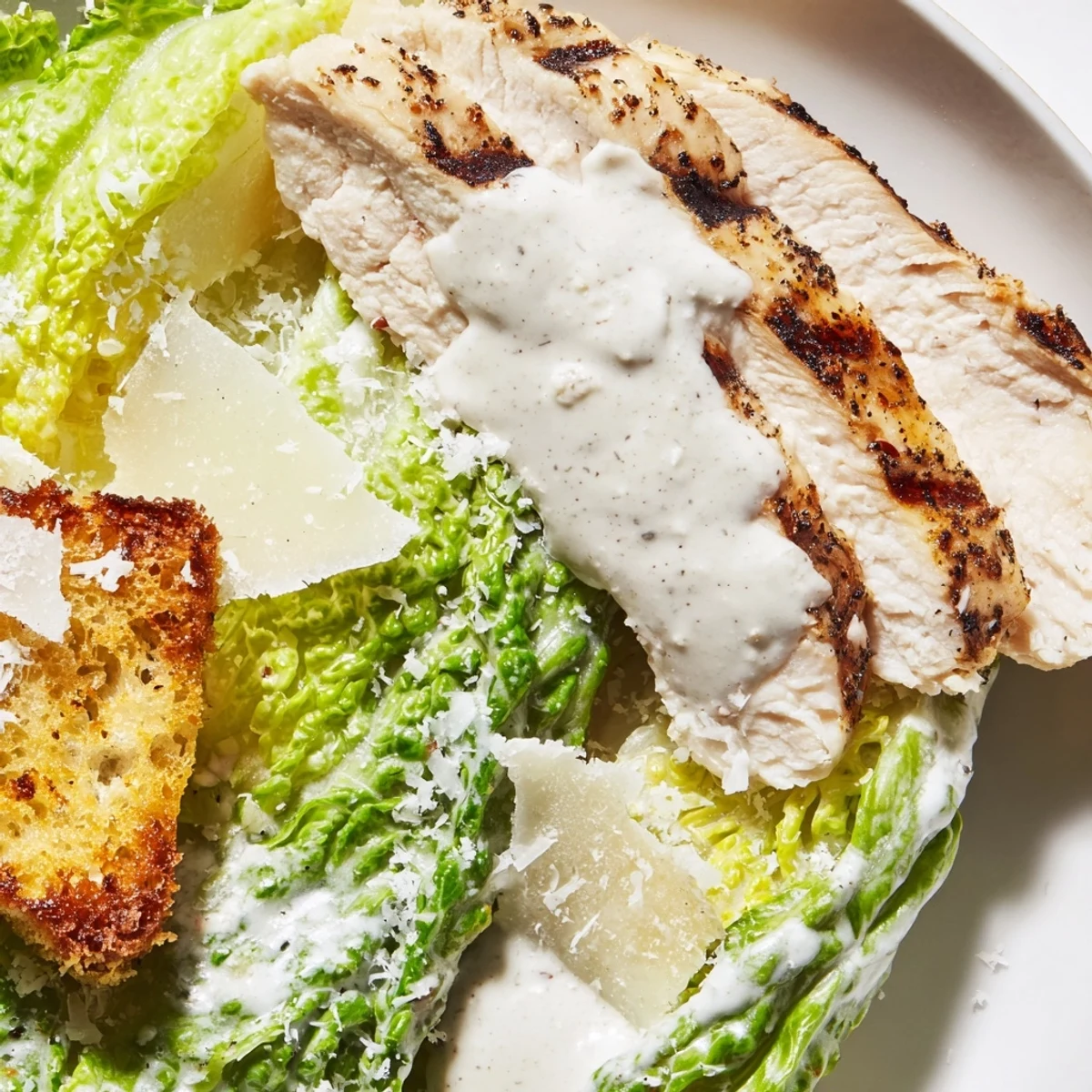 A close-up of creamy Caesar dressing being drizzled over a vibrant Chicken Caesar Salad with golden garlic croutons.