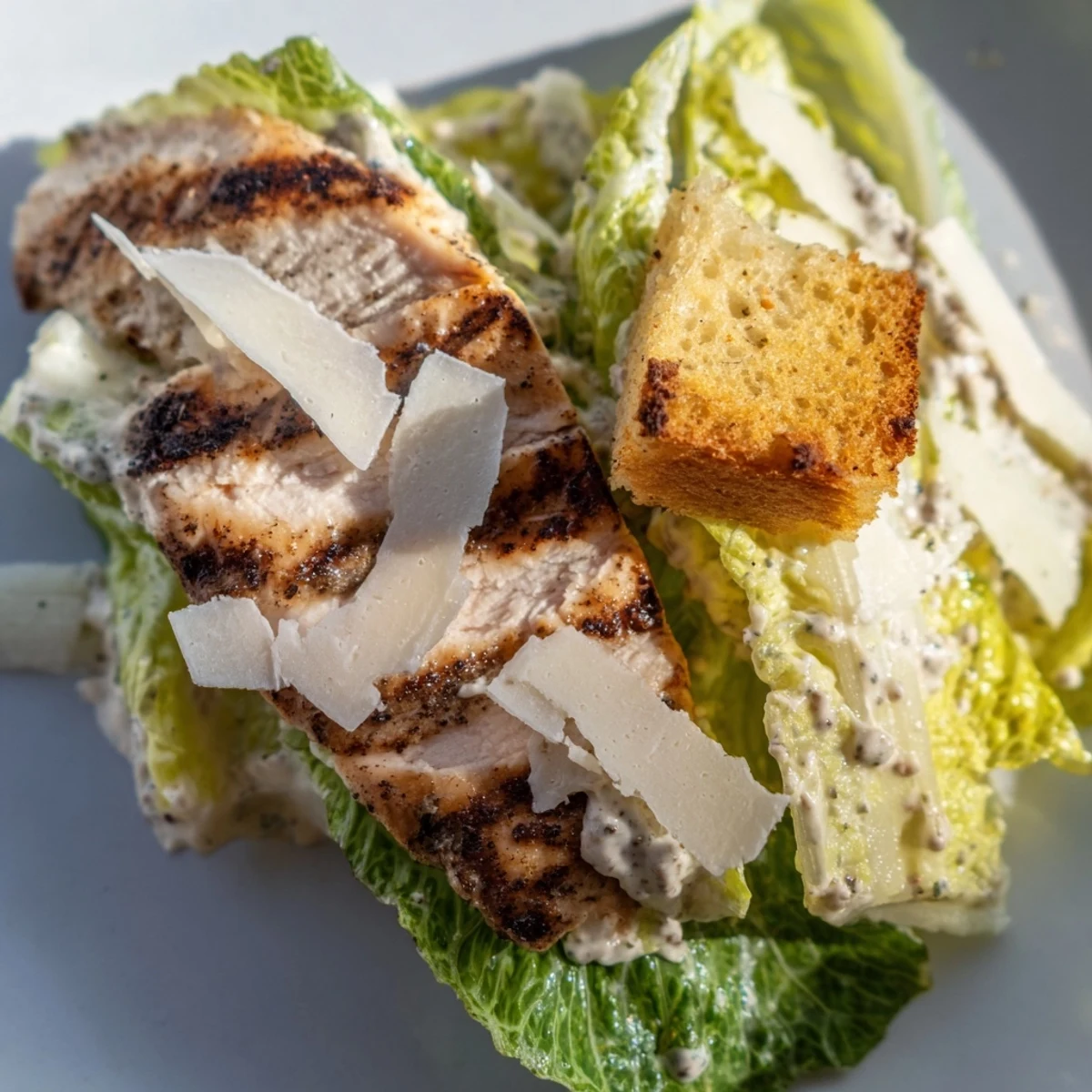 A plated Chicken Caesar Salad garnished with fresh Parmesan shavings, served for a light lunch or dinner.