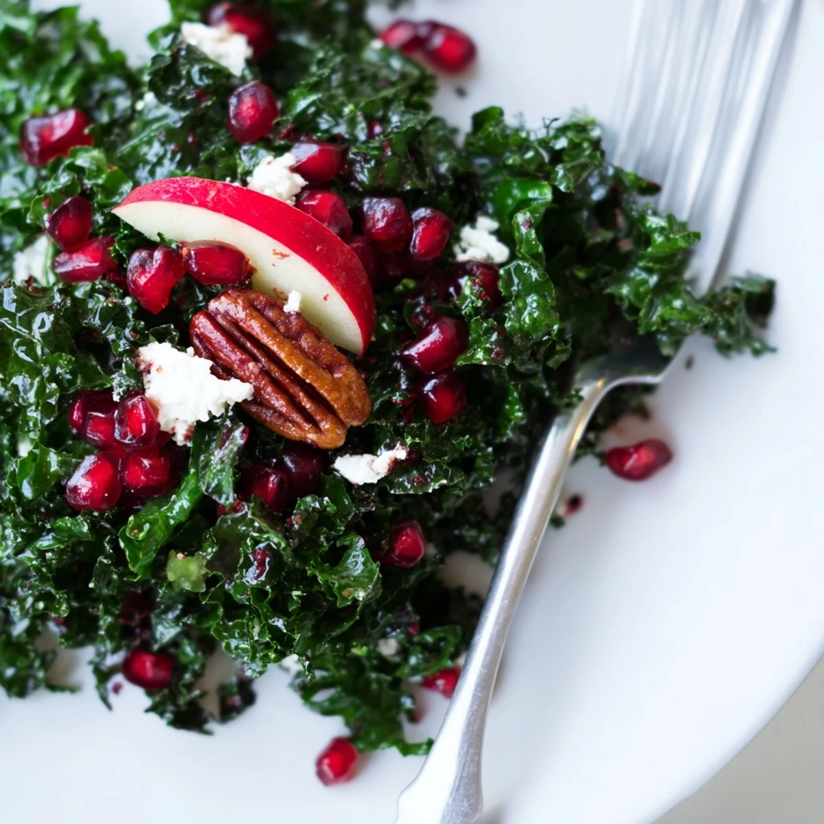A close-up of vibrant Winter Kale Salad with Pomegranate and Pecans, glistening with citrus dressing and topped with sweet red arils.