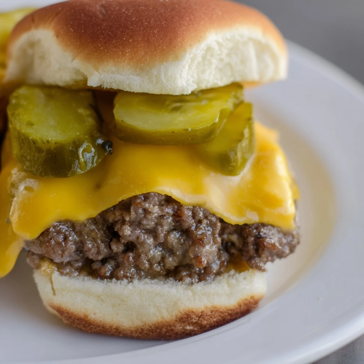 Freshly grilled Beef Sliders with Cheese and Pickles on a platter, with melted cheddar and crisp dill pickles on soft toasted buns.
