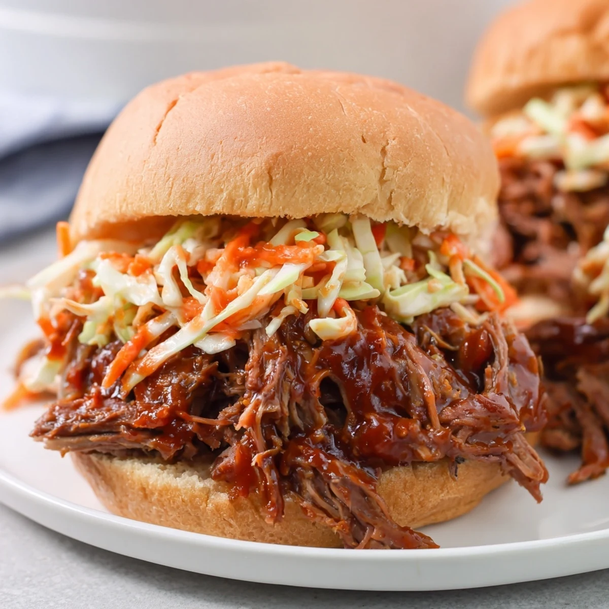 Golden-brown shredded Slow Cooker Pulled Beef Sandwiches piled high on soft buns, topped with creamy coleslaw and barbecue sauce.