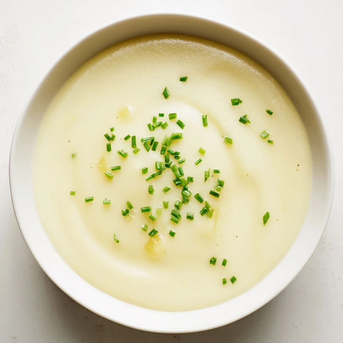 A spoon dips into velvety Creamy Potato Leek Soup with Chives, served beside crusty artisan bread.  