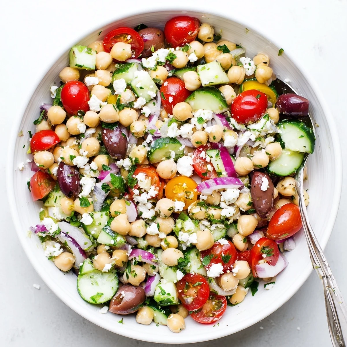 Freshly chopped Mediterranean Chickpea Salad with feta, olives, and cherry tomatoes in a white bowl, ready to serve.