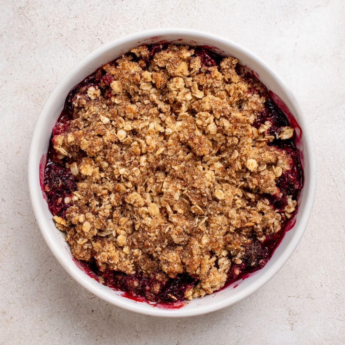 Freshly baked Winter Berry Crumble cooling on a windowsill, cinnamon-scented oats over ruby red winter berries.