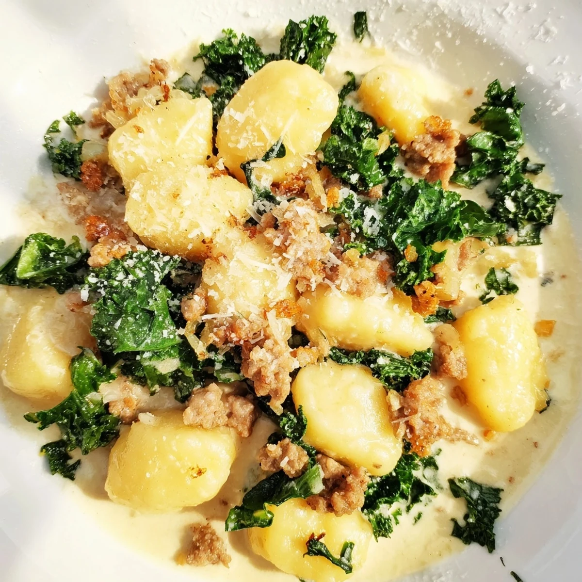 Creamy Gnocchi with Sausage and Kale served in a bowl, topped with fresh Parmesan shavings and a pinch of red pepper flakes.