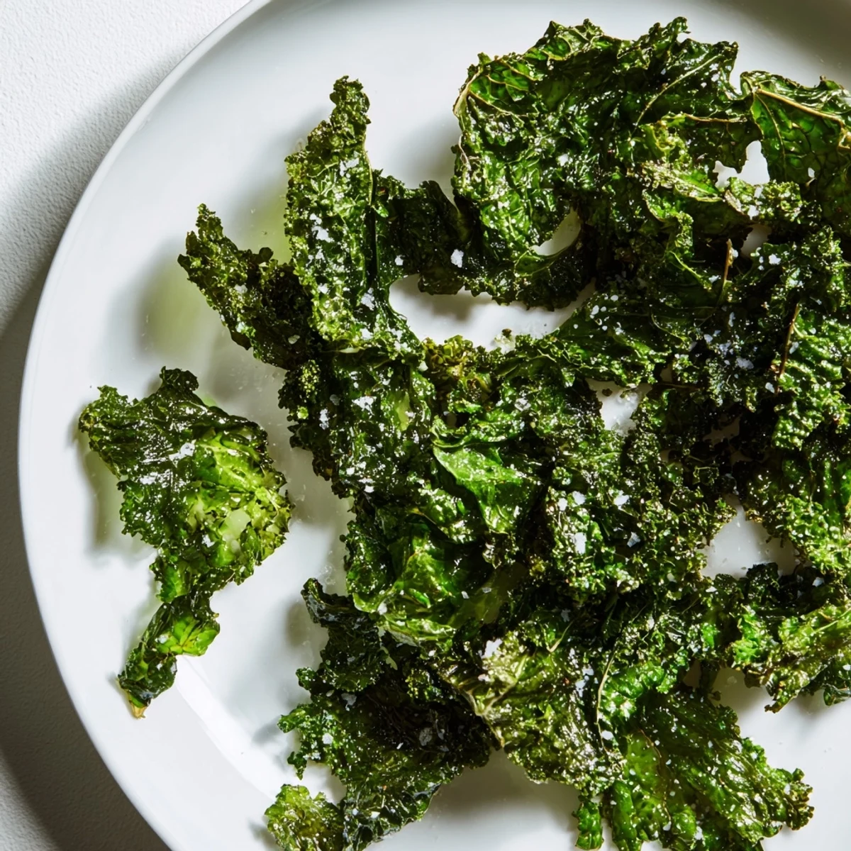 Crispy Green Kale Chips with Sea Salt arranged on a plate with lemon wedges for a tangy snack.