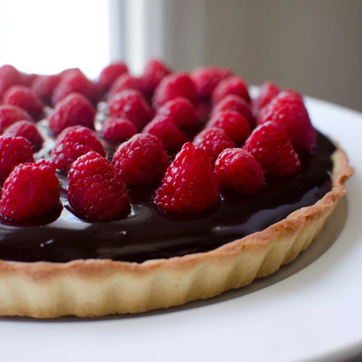 Decadent Chocolate Raspberry Tart garnished with tangy raspberries and a drizzle of raspberry jam glaze on a dessert plate.