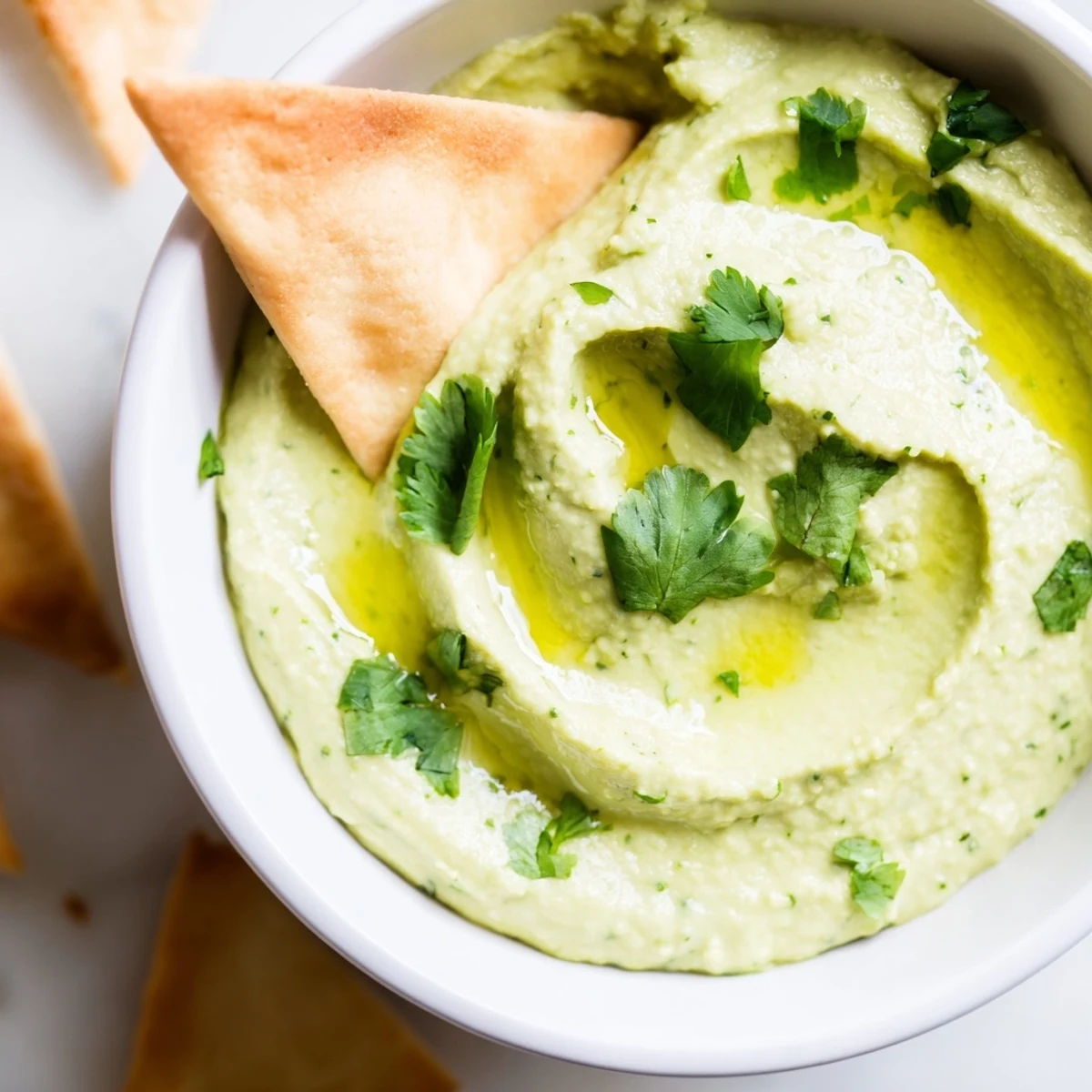 Freshly blended Green Avocado Hummus with Pita Chips garnished with cilantro and olive oil drizzle.