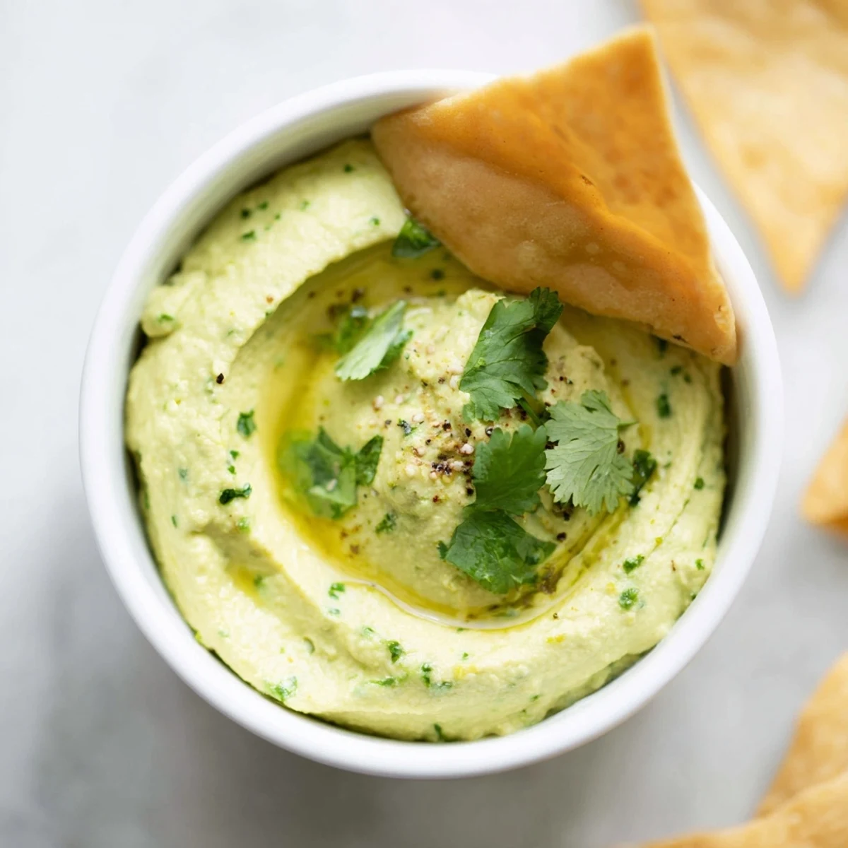 Homemade Green Avocado Hummus topped with paprika and crunchy pita chips on a rustic plate.