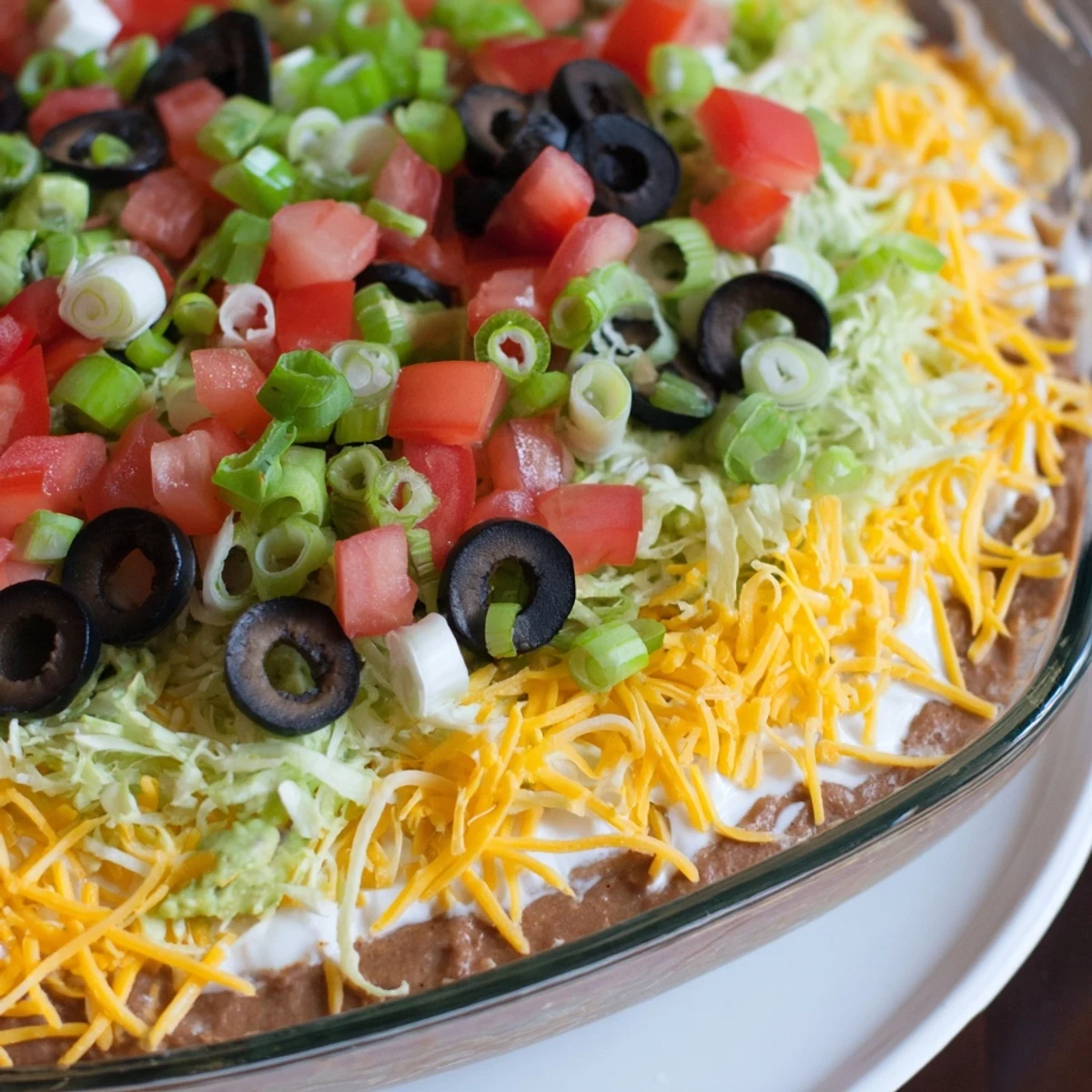 A scoop of Ultimate Seven Layer Taco Dip rests on a chip, showing off the creamy sour cream and bean layers.