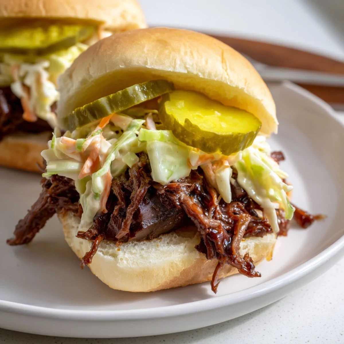 Golden slider buns cradle shredded brisket, topped with creamy coleslaw and dill pickle slices.