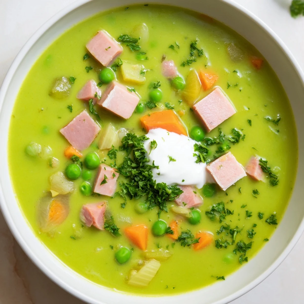 A bowl of vibrant Spring Pea Soup with Ham and Turkey garnished with fresh parsley and a swirl of creamy crème fraîche.  
