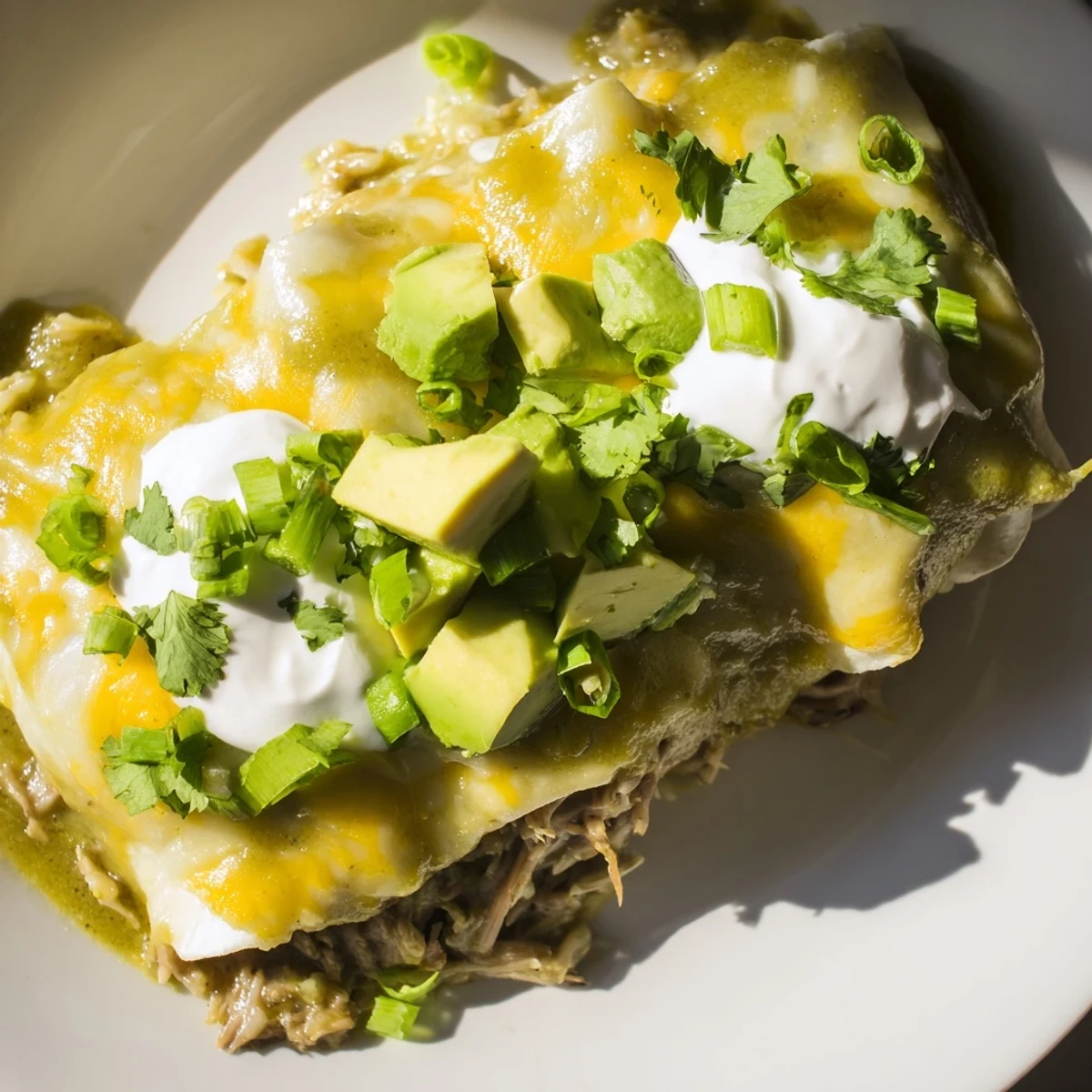 A close-up of rolled Beef Enchiladas with Green Sauce topped with sour cream.