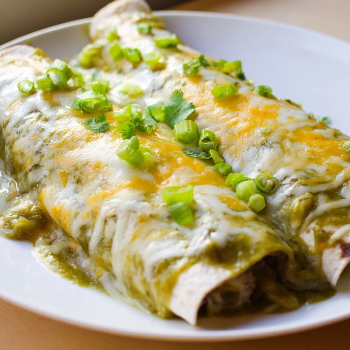 Freshly baked Beef Enchiladas with Green Chili Sauce served with cilantro garnish and lime wedges.