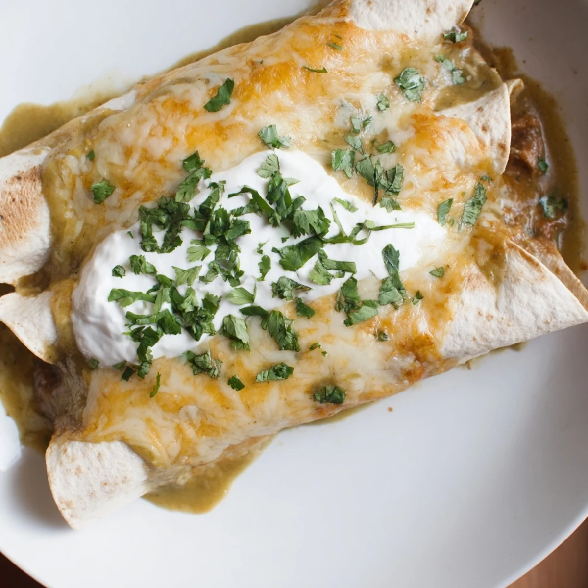 A close-up of Beef Enchiladas with Green Sauce, served with creamy sour cream and lime wedges.