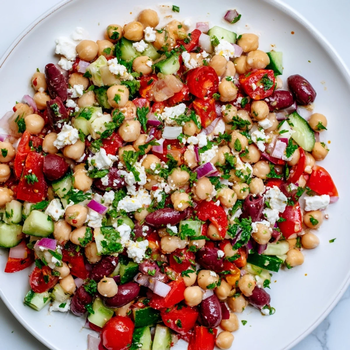 A close-up of vibrant Mediterranean Dense Bean Salad brimming with chickpeas, feta, and fresh herbs on a white plate.