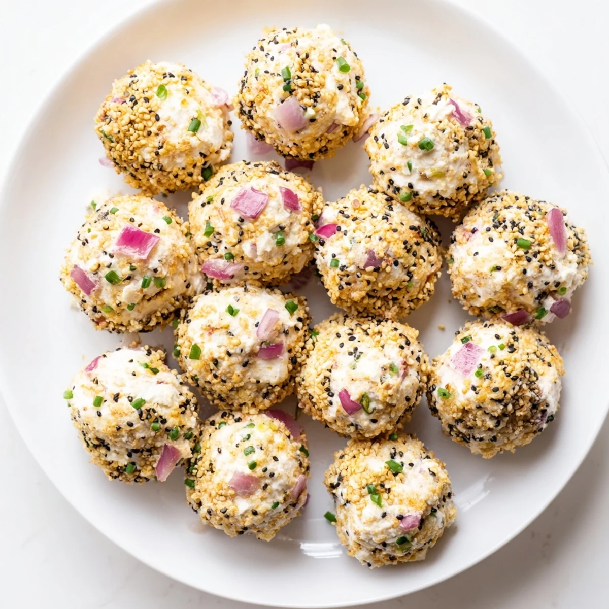 Everything Bagel Cottage Cheese Bites arranged on a white platter with fresh chives and red onion garnish, ready to serve as a high-protein appetizer.