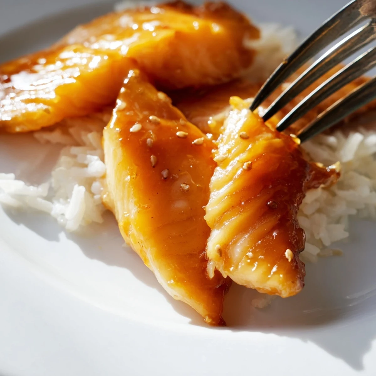 A vibrant serving of Sweet & Spicy Cod Strips with Chili-Garlic Drizzle over Rice, featuring tender fish pieces drizzled with spicy red oil and garnished with sesame seeds.