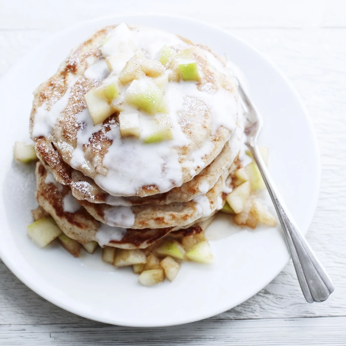 Fluffy Apple Fritter Pancakes studded with tender cinnamon apples, topped with a sweet glaze on a breakfast plate.