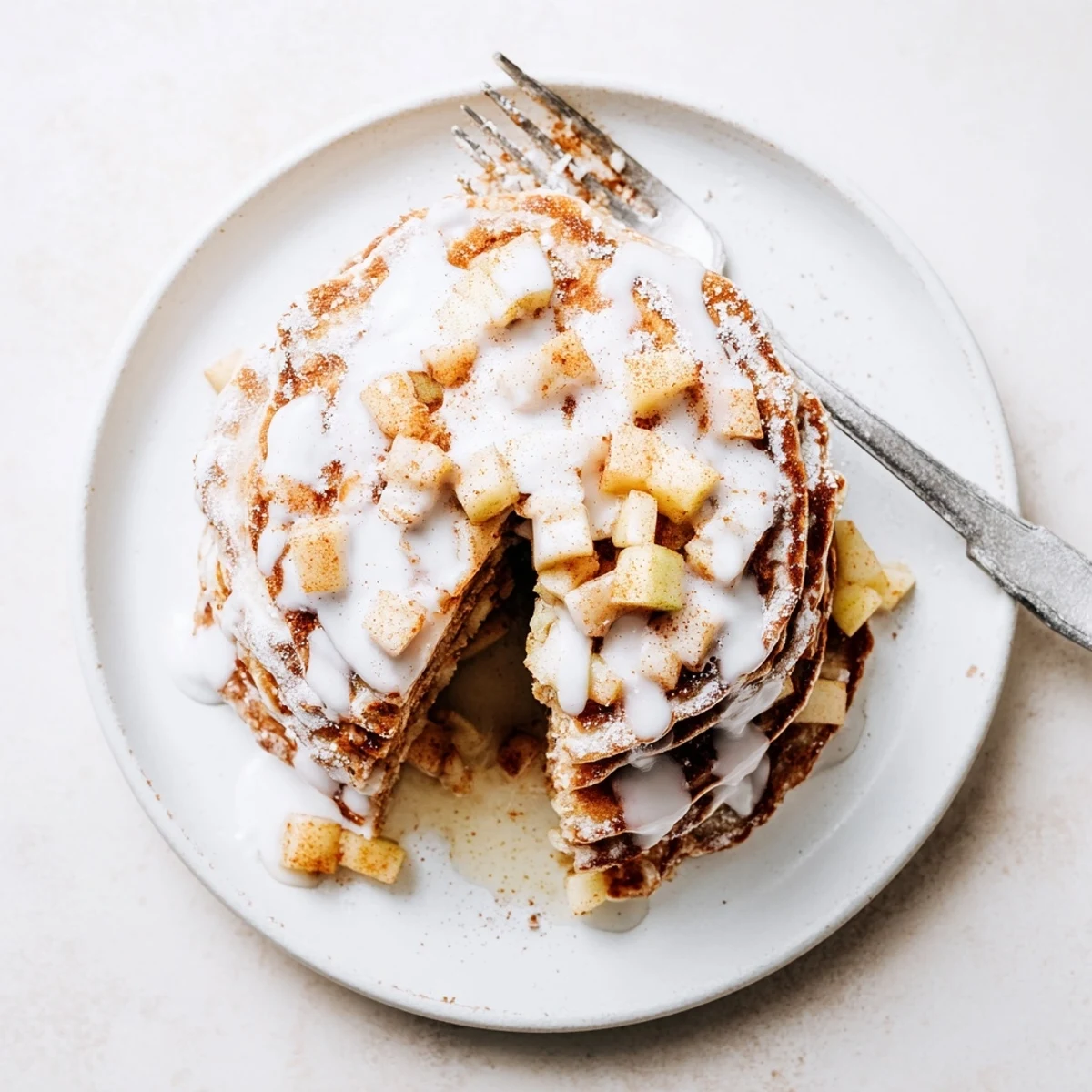 Golden brown Apple Fritter Pancakes with diced apples and warm spice, stacked high and drizzled with vanilla glaze.