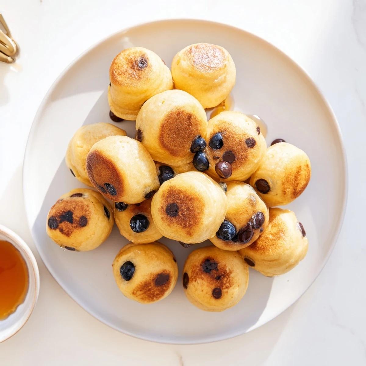 Bite-sized Pancake Poppers filled with blueberries served warm on a white plate with syrup.