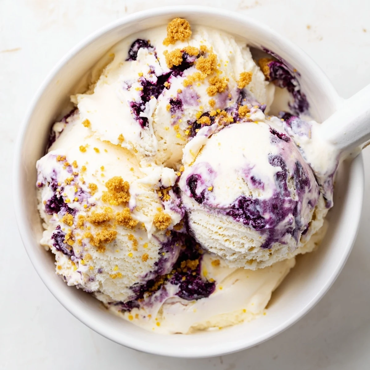 A scoop of Lemon Blueberry Cheesecake Ice Cream with blueberry swirls and graham cracker crumbs.