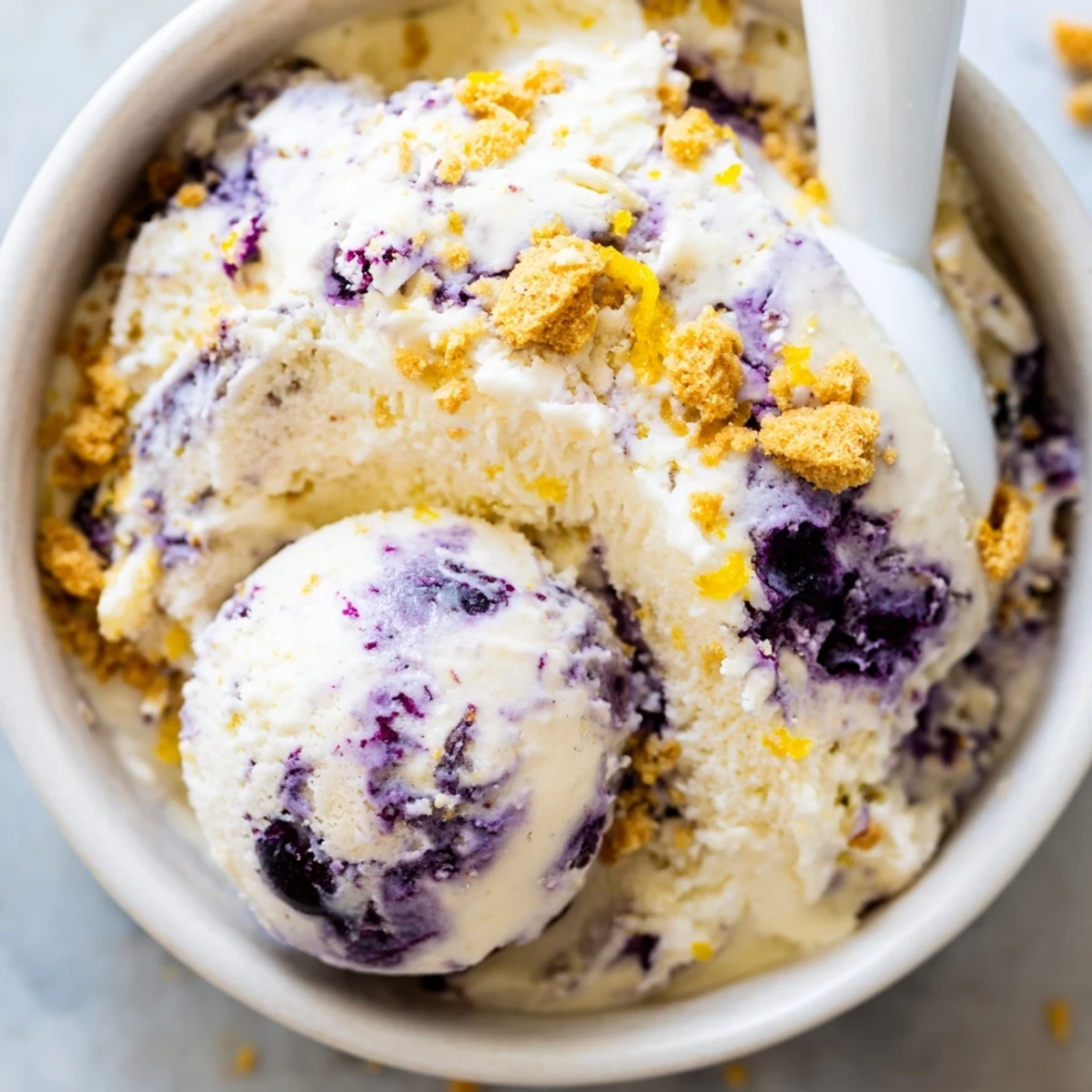 Serving suggestion for Lemon Blueberry Cheesecake Ice Cream with a waffle cone and lemon zest.