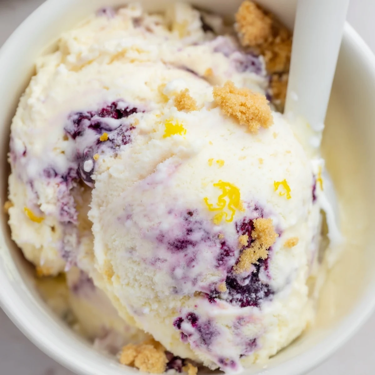 Close-up of creamy Lemon Blueberry Cheesecake Ice Cream in a bowl with fresh blueberries.