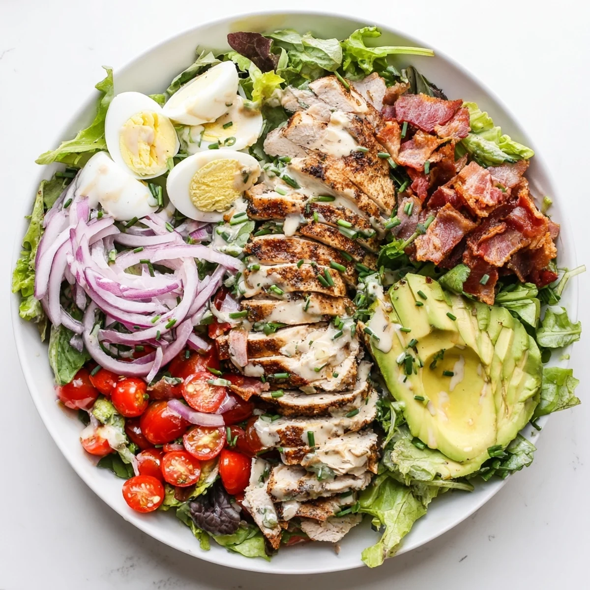 Grilled chicken slices and crispy bacon over mixed greens in a Paleo Grilled Chicken Cobb Salad With Honey Dijon Dressing.