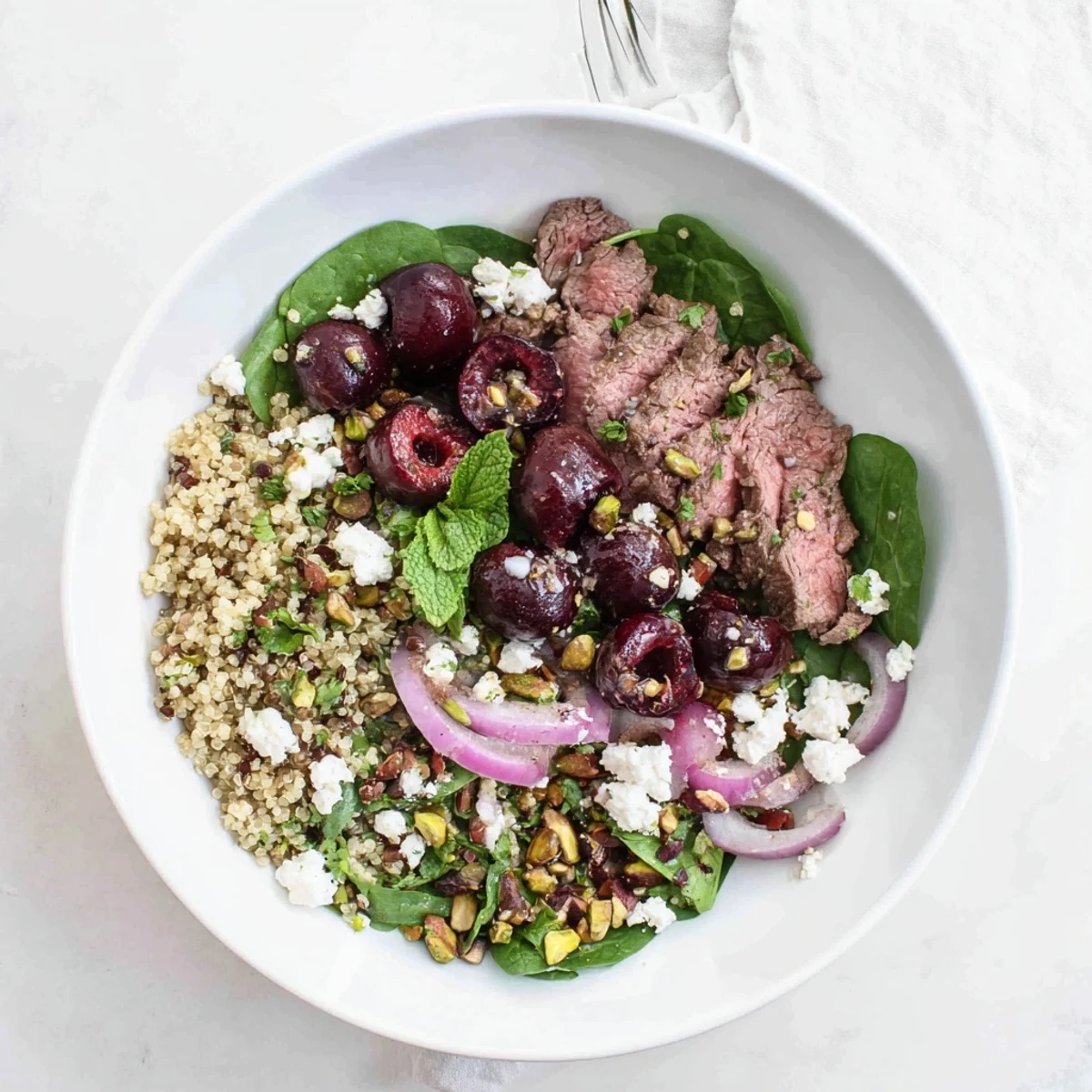 Mediterranean-inspired cherry quinoa salad bowl with tender lamb, spinach, and zesty lemon dressing