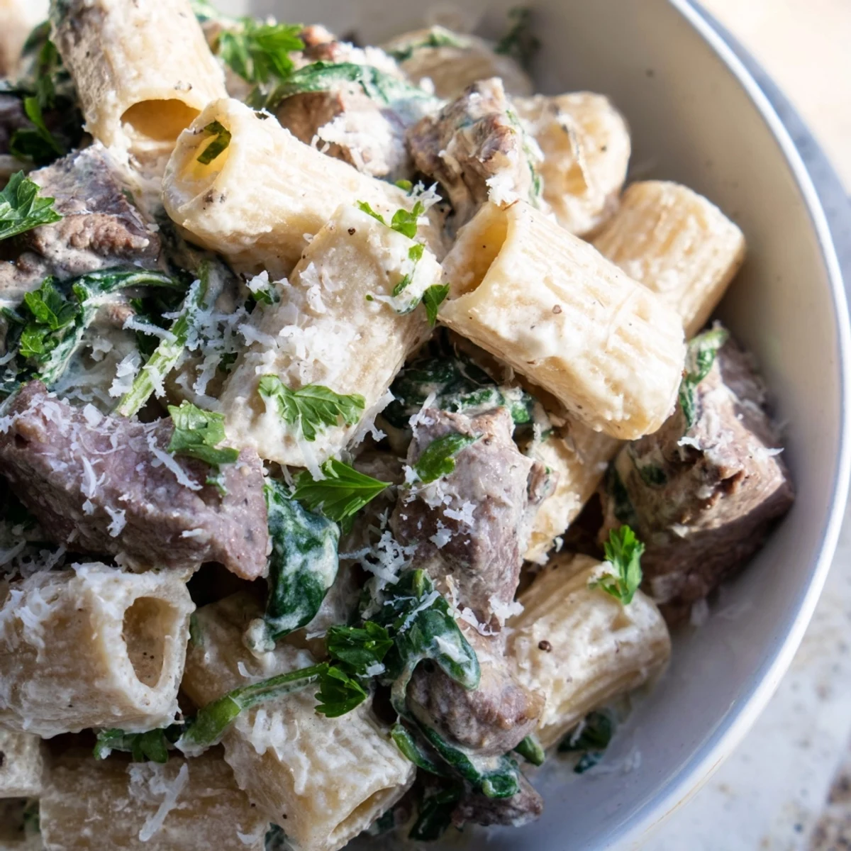 Creamy high protein beef pasta tossed in a rich white sauce with tender sliced beef pieces and wilted spinach.