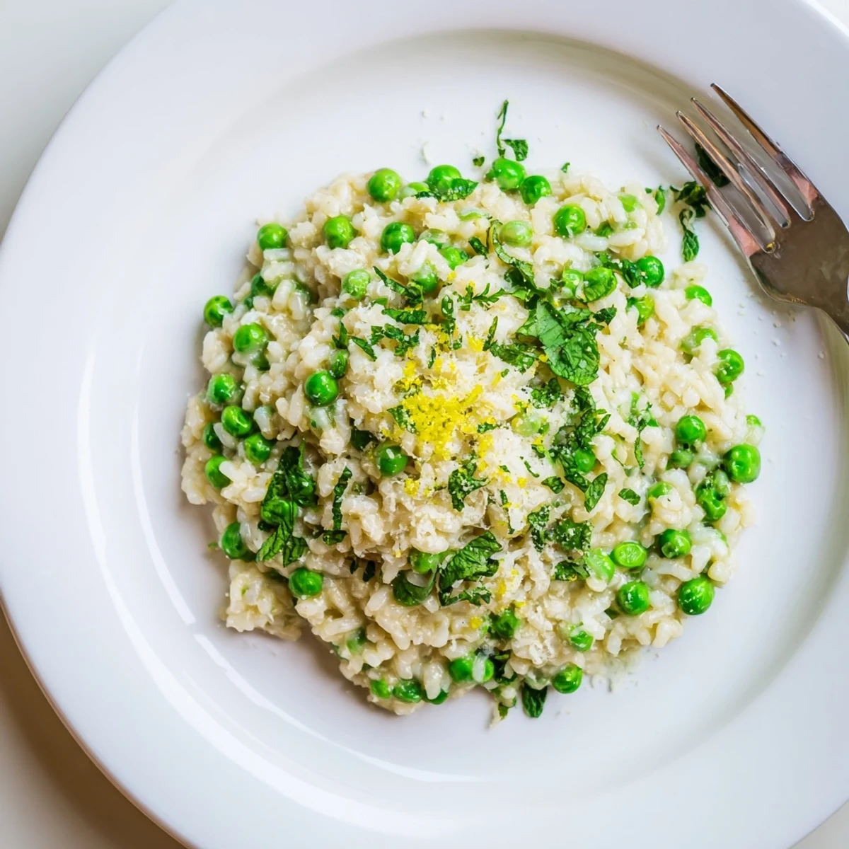 Vibrant spring pea risotto plated with delicate mint sprigs and lemon zest garnish on rustic wooden surface