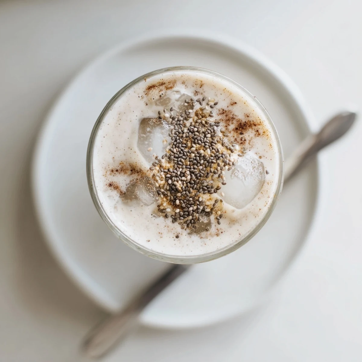Golden Greek yogurt banana smoothie poured into a tall glass with ice cubes on a wooden counter