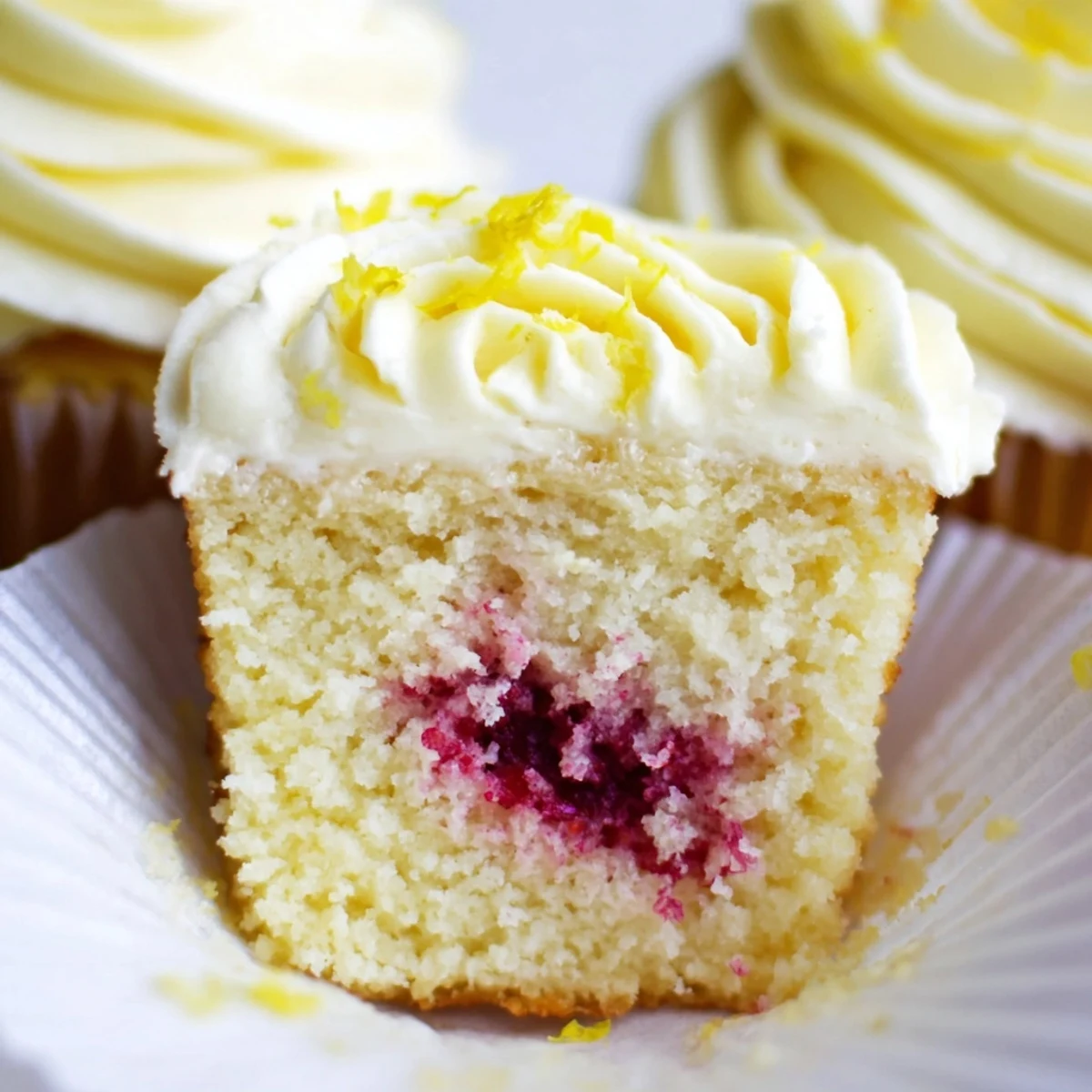 Zesty lemon cupcakes with hidden raspberry jam filling and smooth buttercream on white plates
