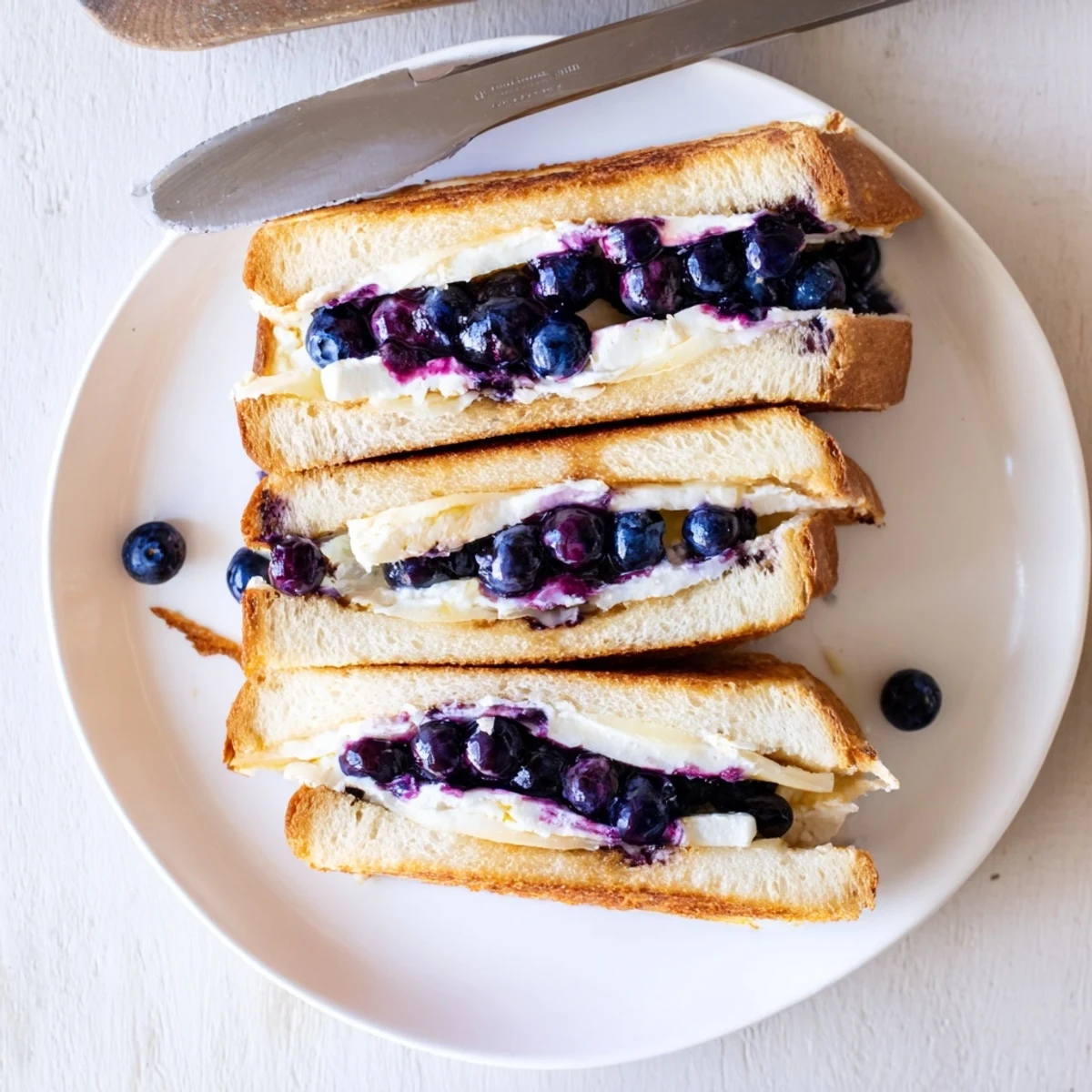 Sliced blueberry grilled cheese revealing oozing cheese and burst fruit on white plate