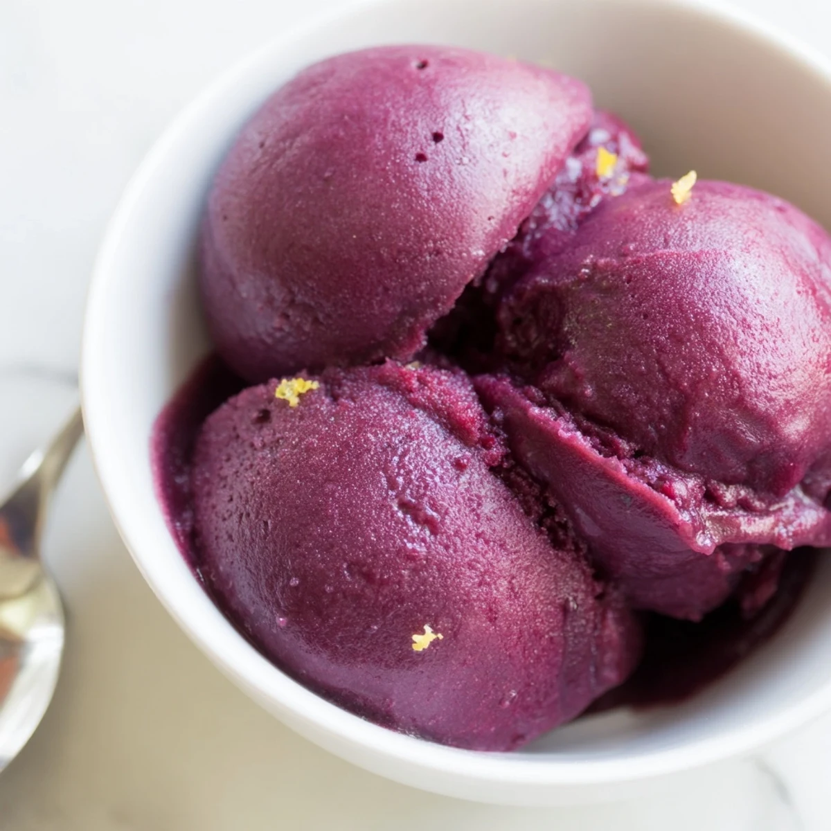 Creamy swirls of dairy-free blueberry lemon sorbet melting slightly in a dessert bowl on a wooden table