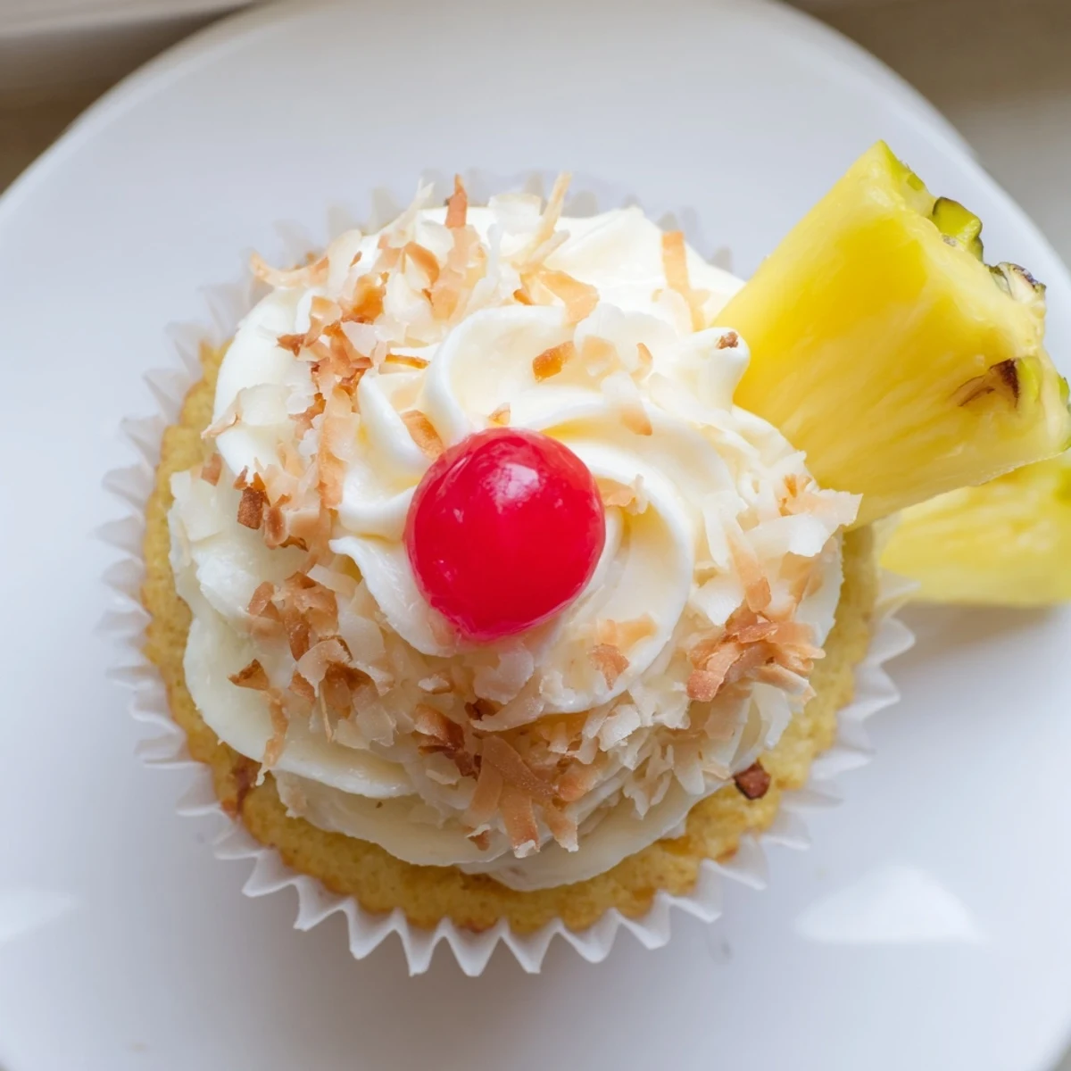 Golden Pina Colada cupcakes topped with fluffy white coconut frosting and garnished with maraschino cherries