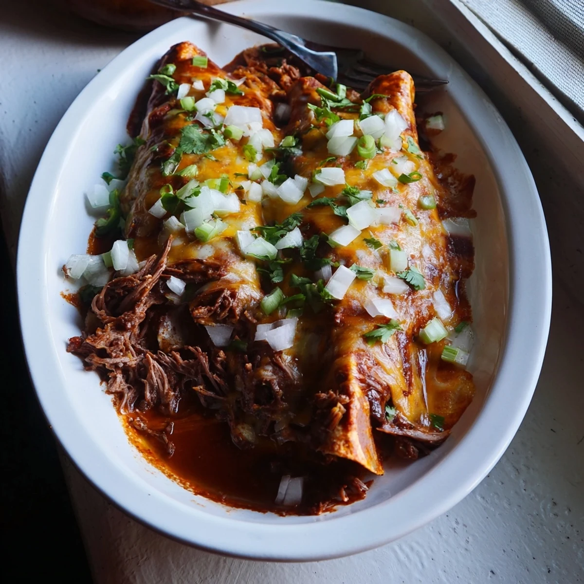 Tender beef birria enchiladas garnished with fresh cilantro and lime wedges