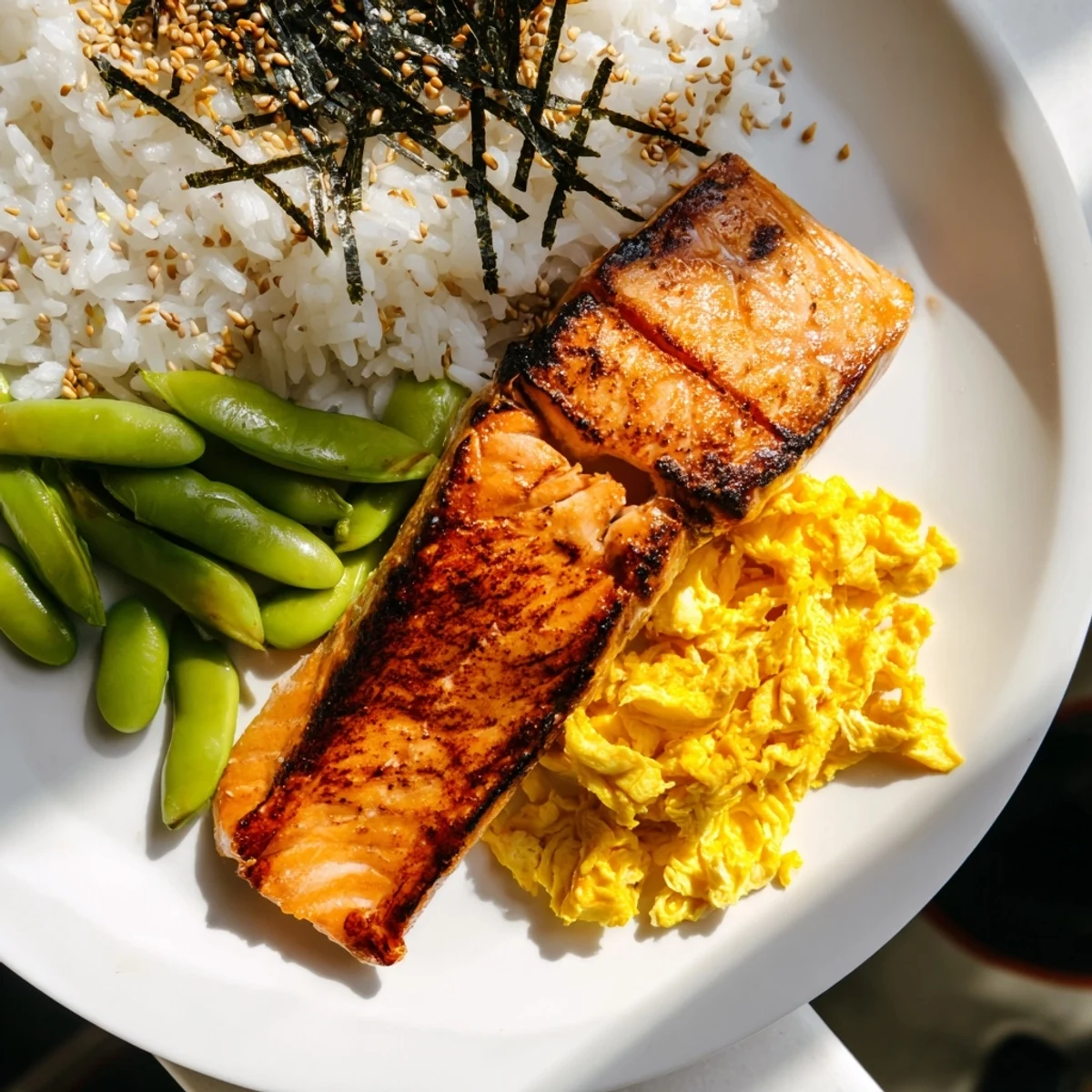 Healthy Japanese breakfast bento featuring savory fish, fluffy white rice, marinated vegetables, and sliced avocado in a portable container