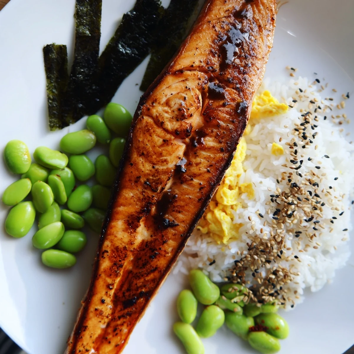 Nourishing bento box with grilled fish, scrambled eggs, pickled carrots, cucumber, and apple slices served over short-grain rice