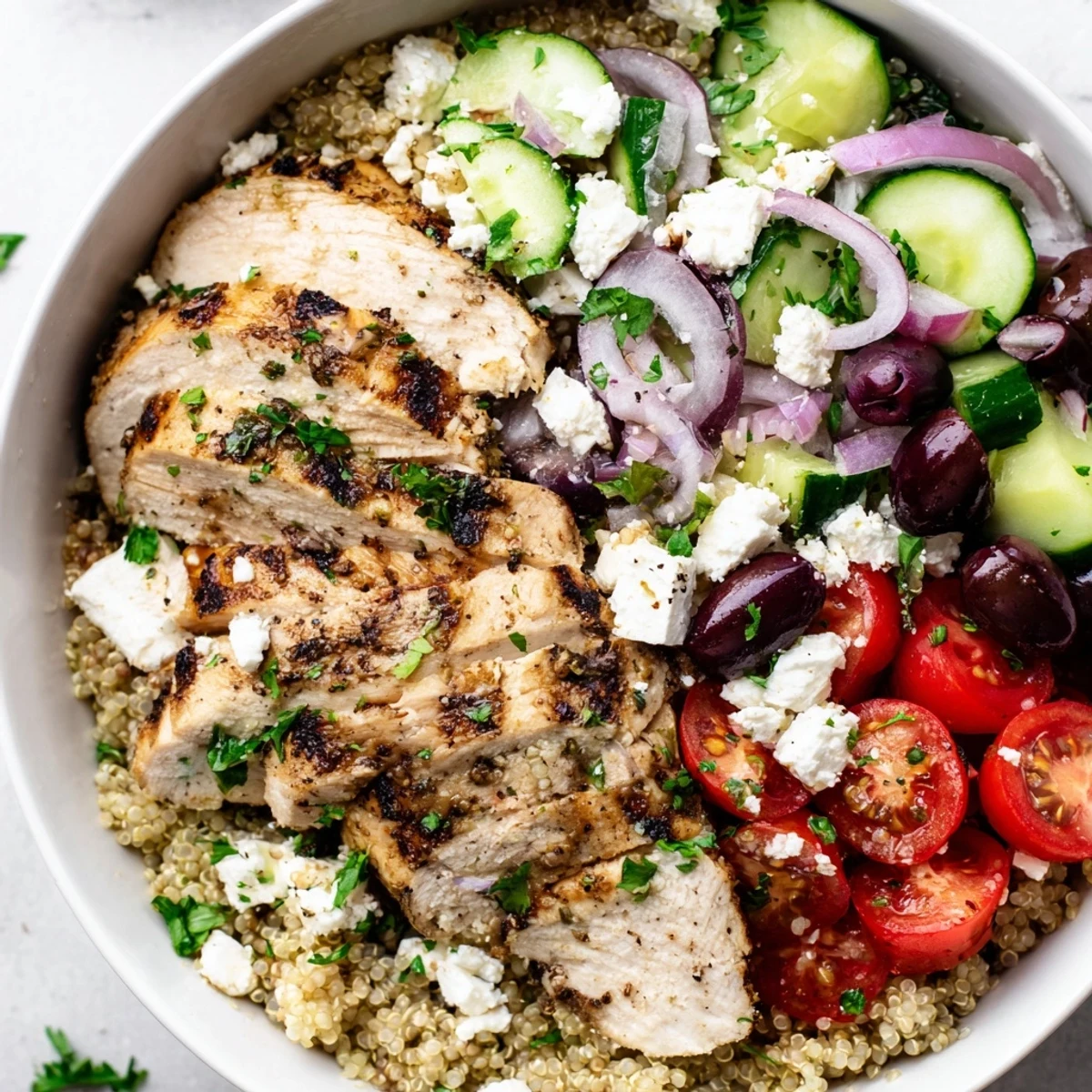 Colorful Mediterranean chicken quinoa bowl topped with crisp vegetables and crumbled feta cheese