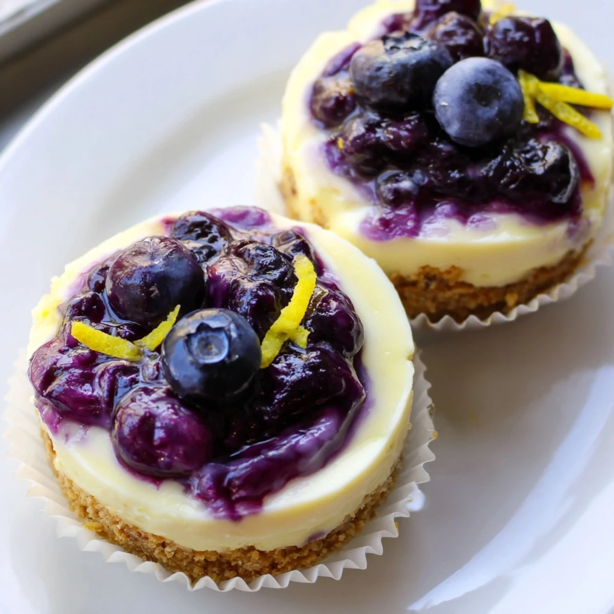 Mini lemon blueberry cheesecakes topped with vibrant purple compote on a rustic dessert plate