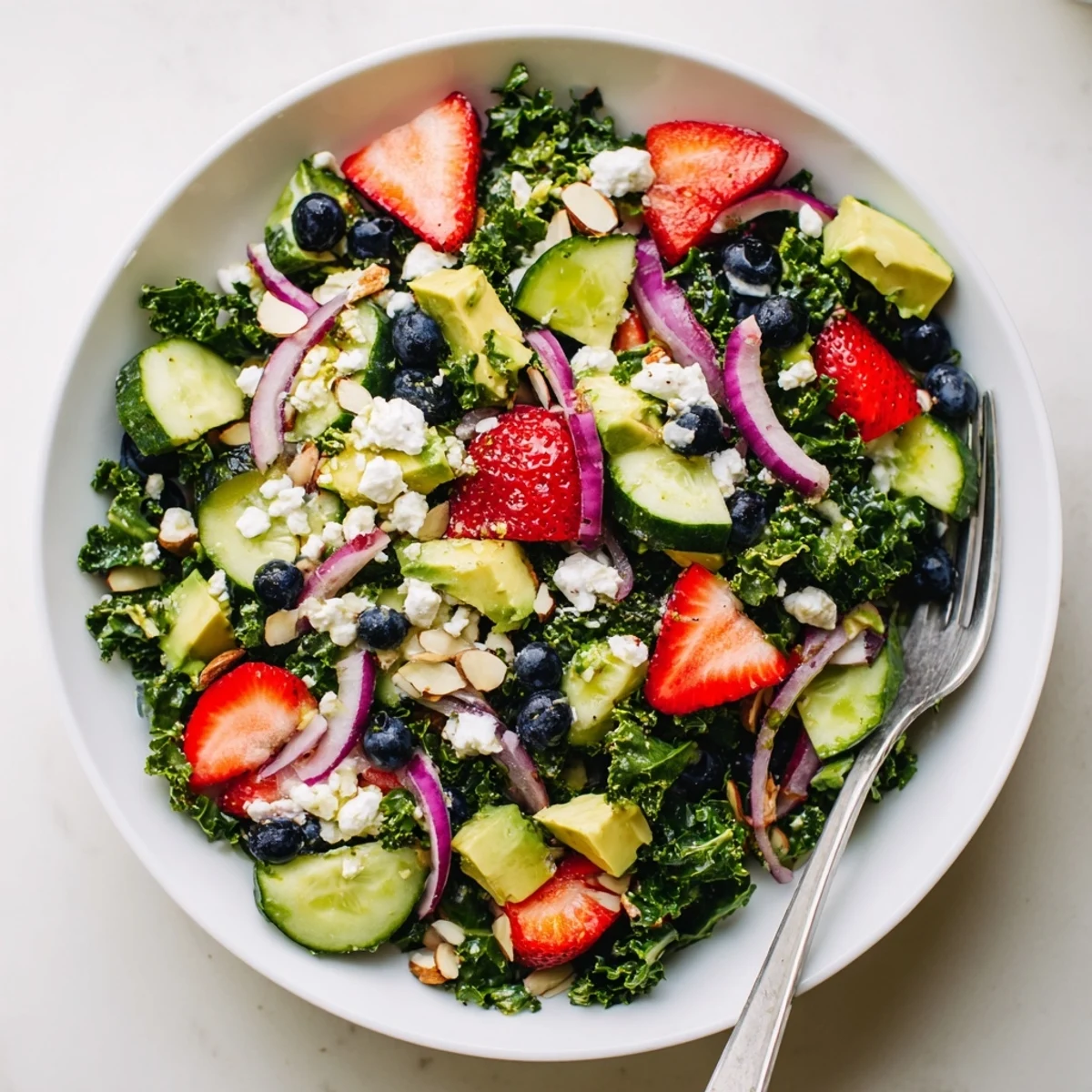 Colorful summer kale salad topped with feta, strawberries, and toasted almonds in a shallow bowl.