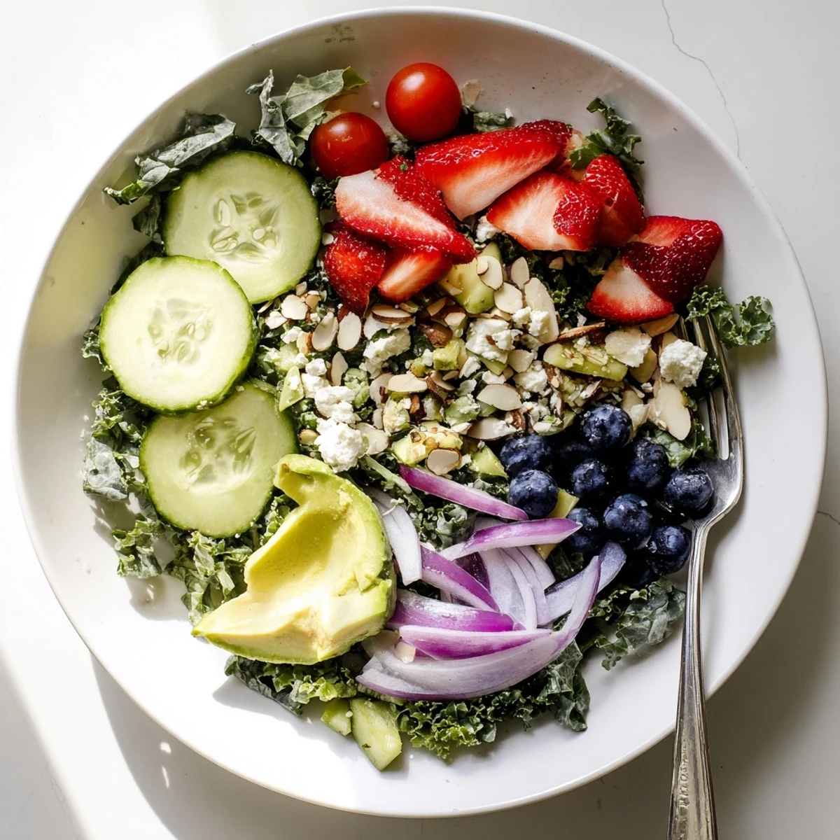 Hearty summer kale salad arranged on a white plate with juicy fruit and crunchy almonds.