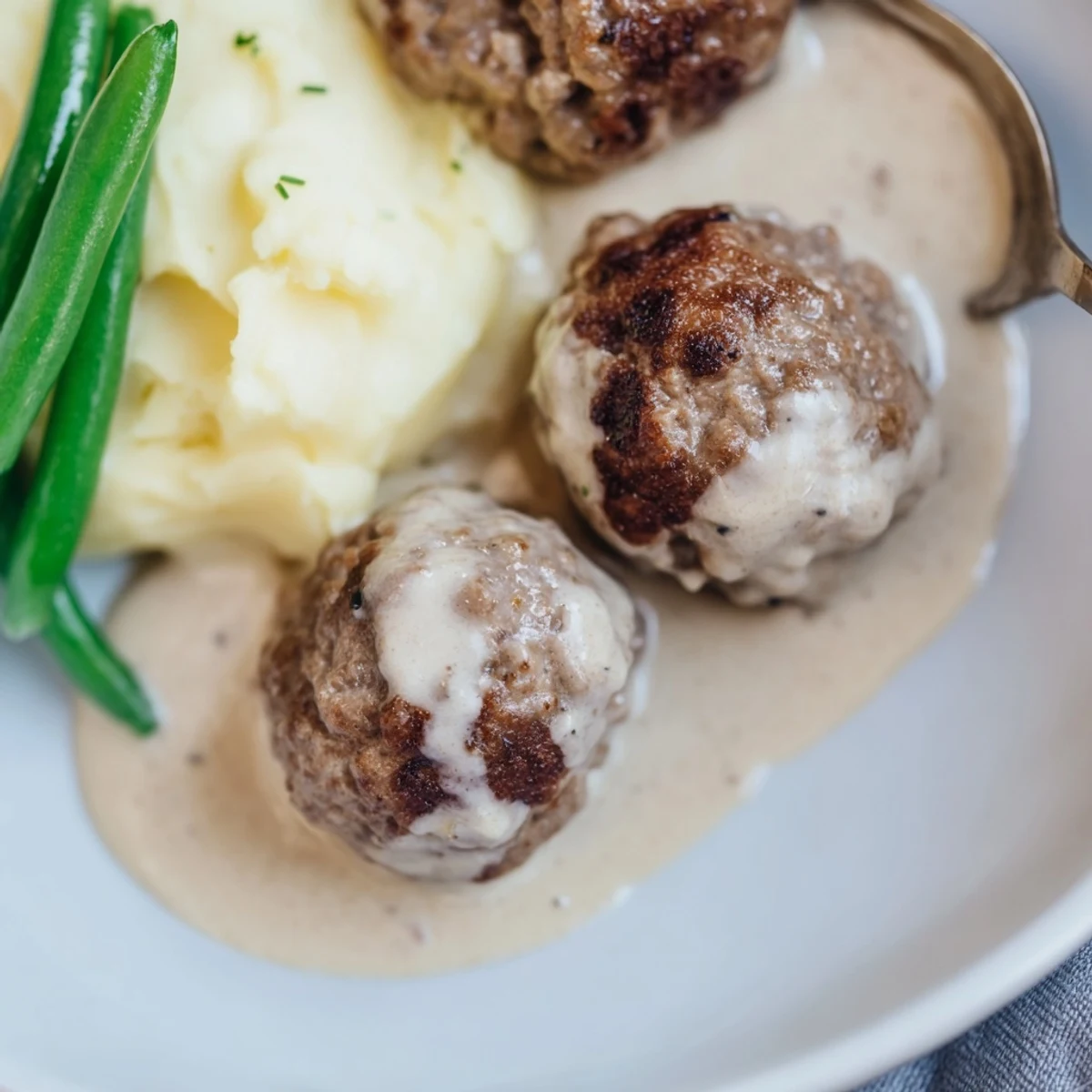 Plate of Homemade Ikea Meatballs glistening with sauce, garnished with lingonberry jam