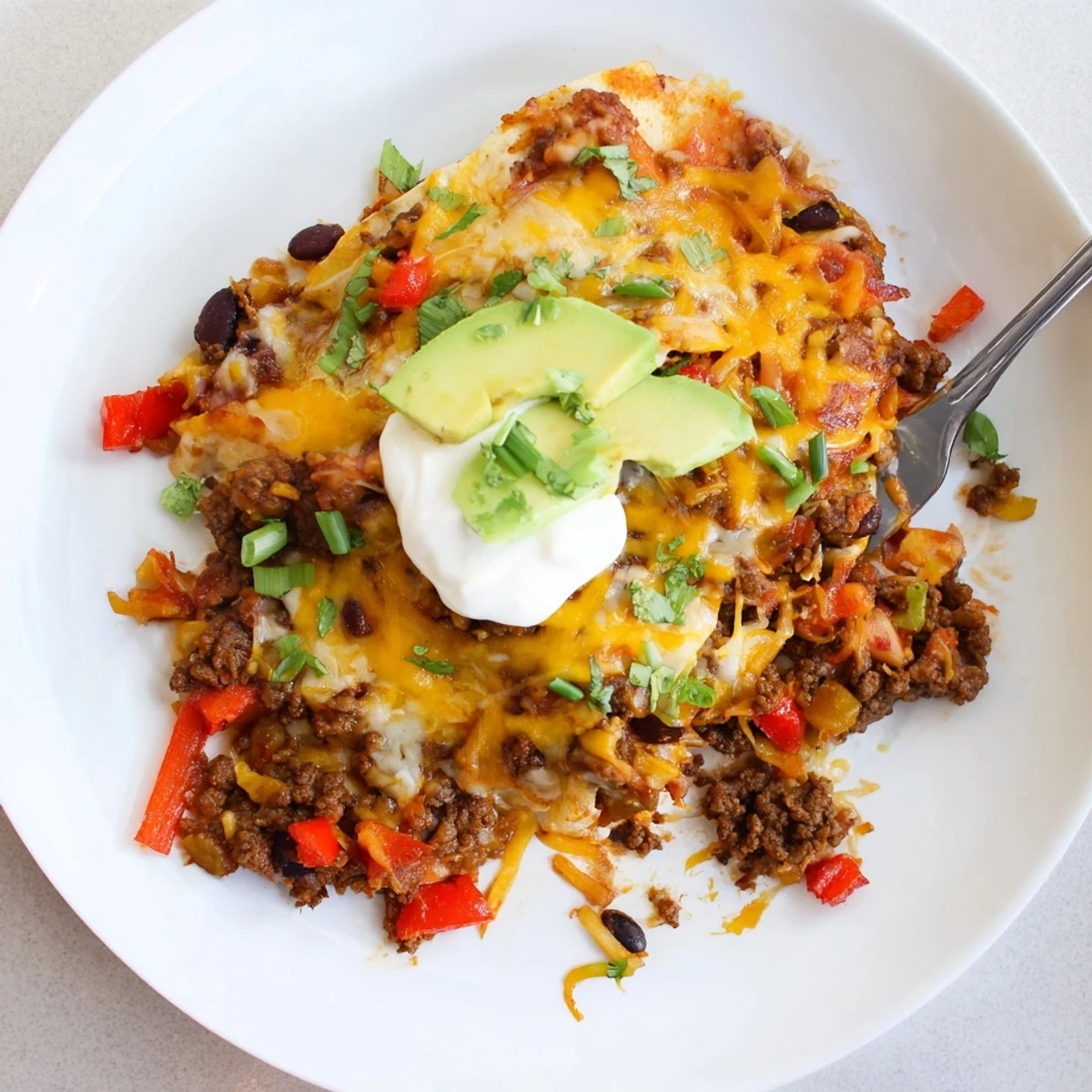 Beef Skillet Enchiladas topped with avocado, green onions, and creamy sour cream