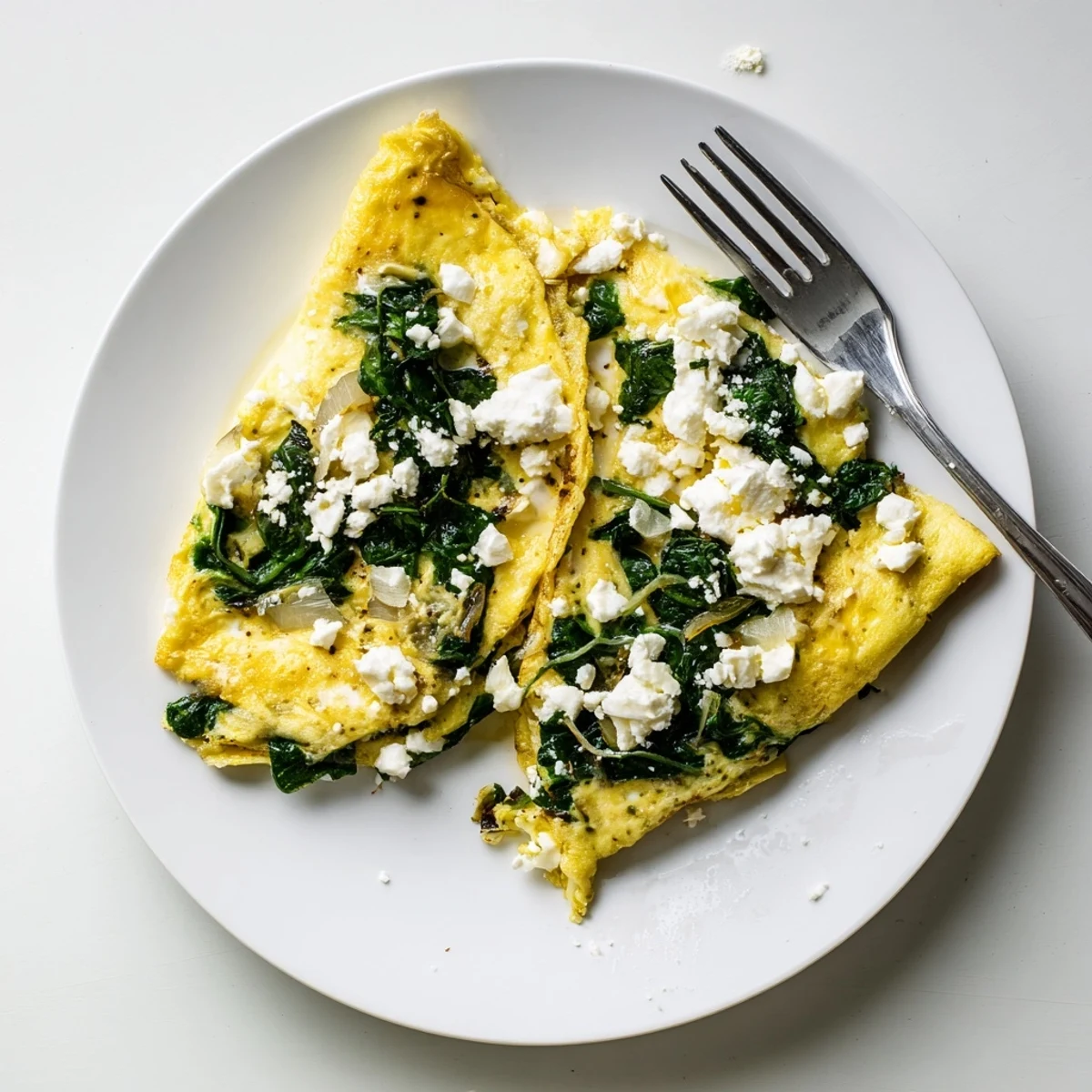 Golden spinach feta omelet recipe folded over melted cheese and wilted greens