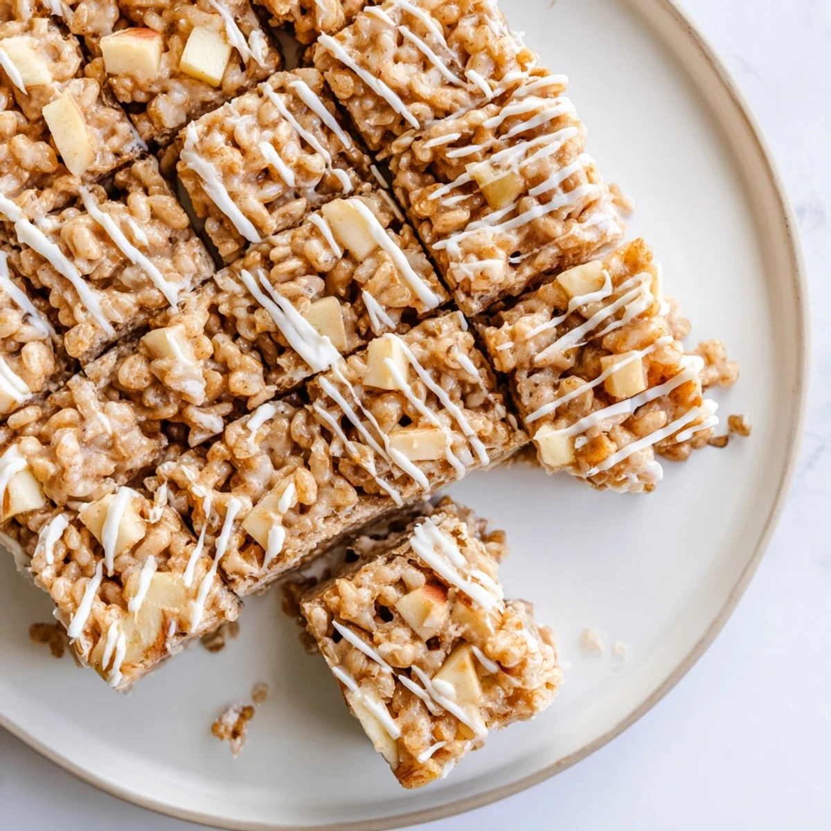 Golden Apple Pie Rice Krispie Treats topped with melted white chocolate drizzle on a white plate