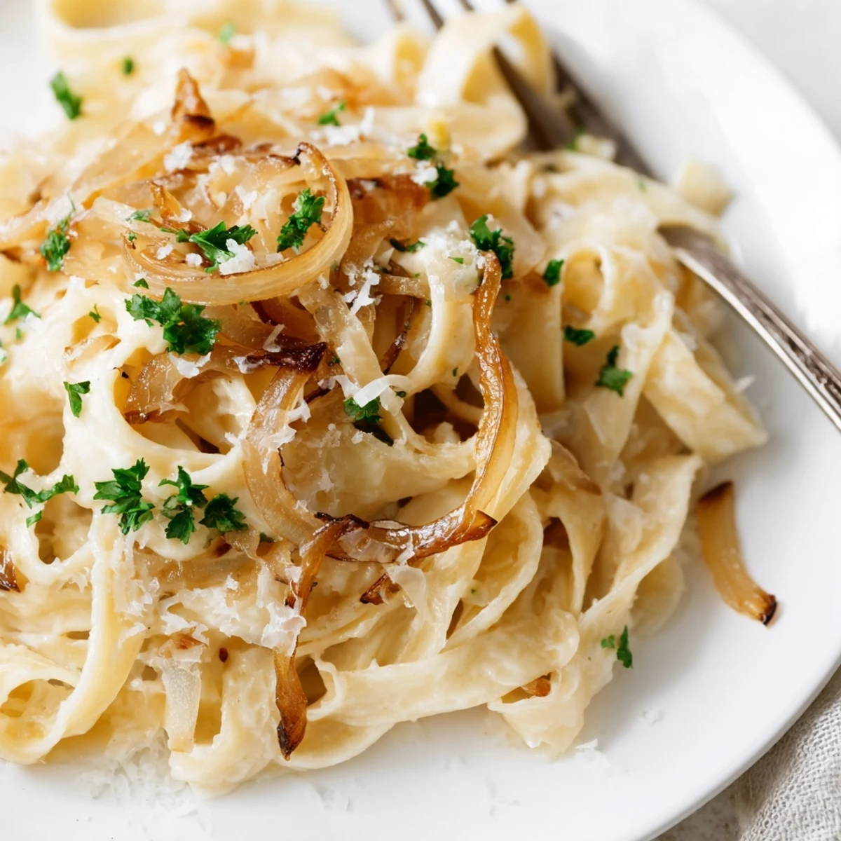 Golden caramelized onion cream pasta twirled on a white plate with fresh parsley garnish