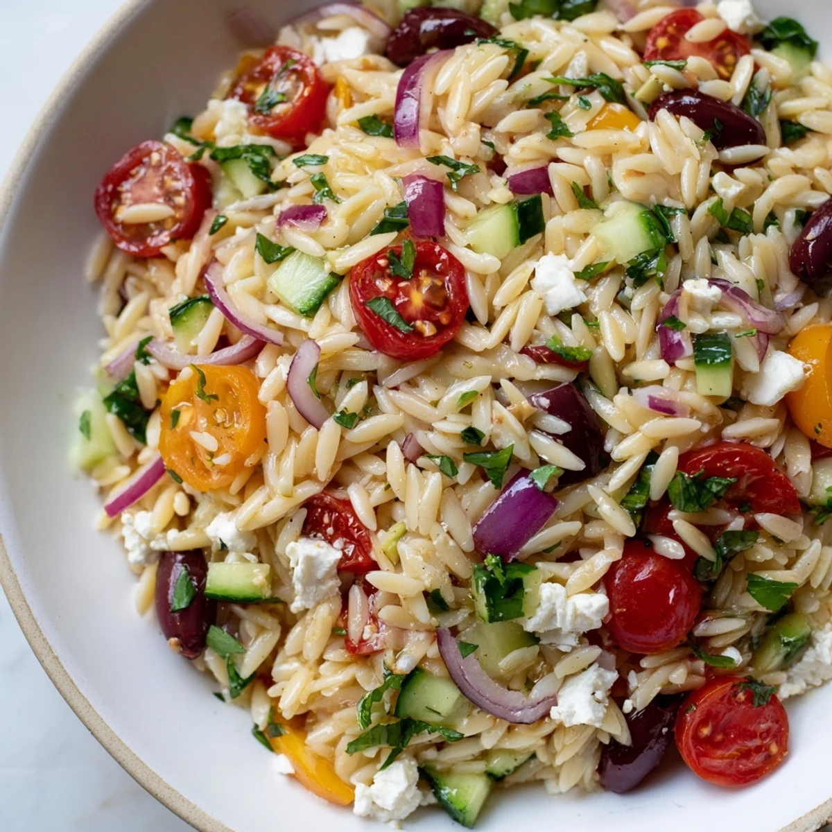 Juicy Mediterranean orzo pasta salad topped with crumbled feta and fresh herbs in a bright white serving bowl